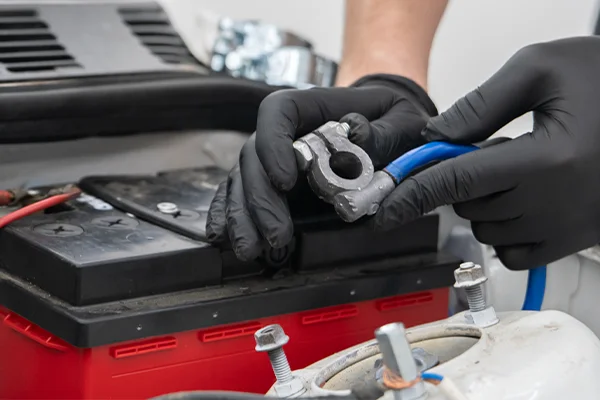 technician installing battery cable on red car battery