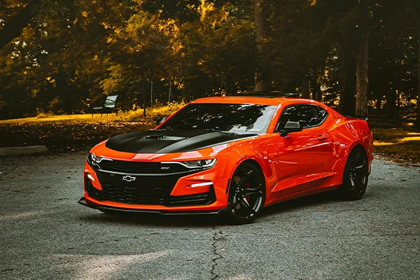 Orange Chevrolet Camaro parked on road in forest